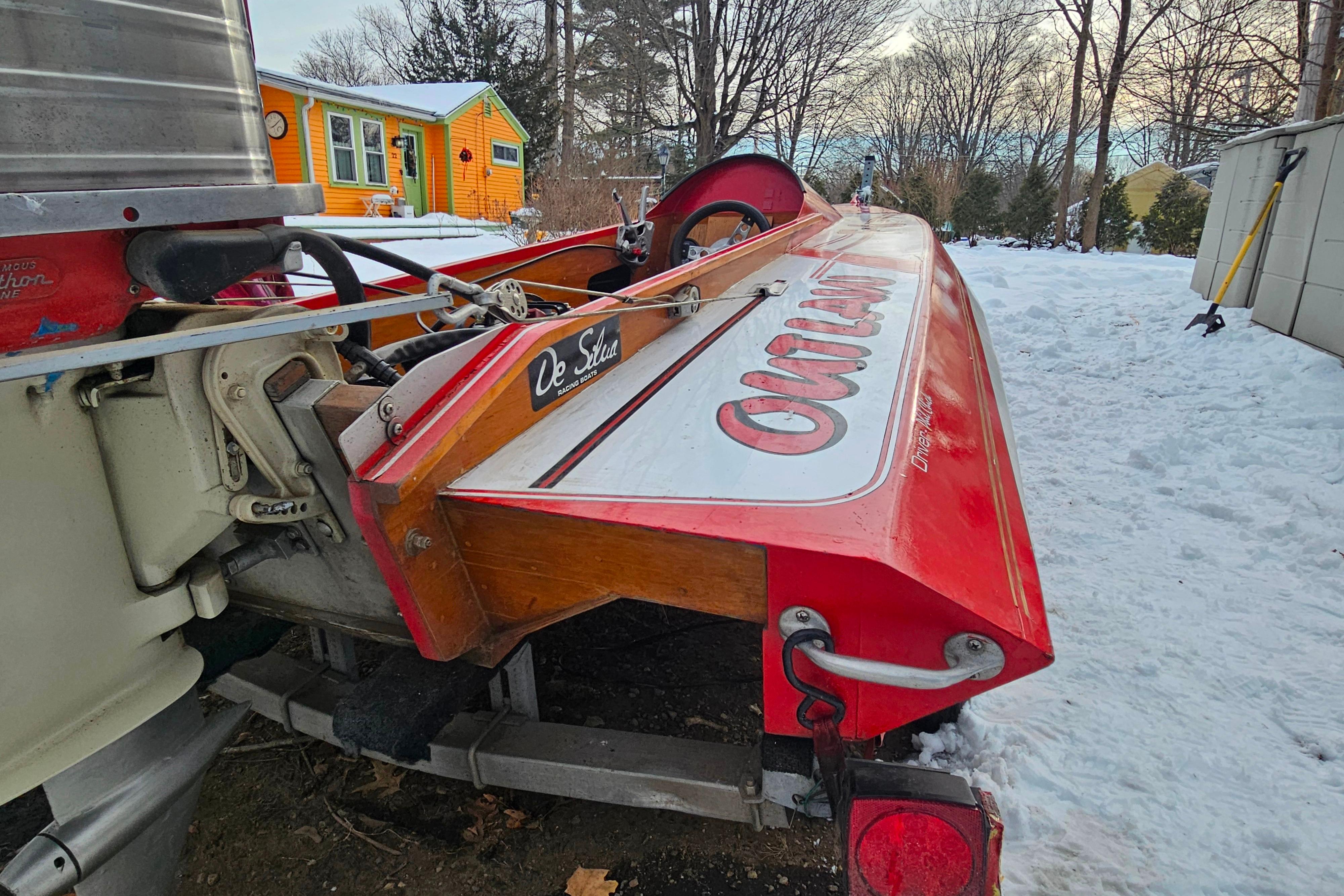 1987 De Silva F Class Race boat in snowy yard, vibrant orange house in background.