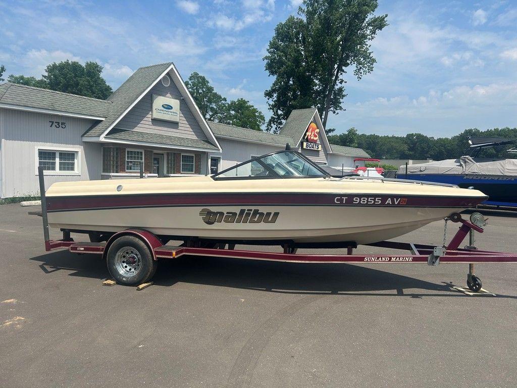 1999 Malibu Sunsetter VLX boat on trailer, parked outside a building on a sunny day.