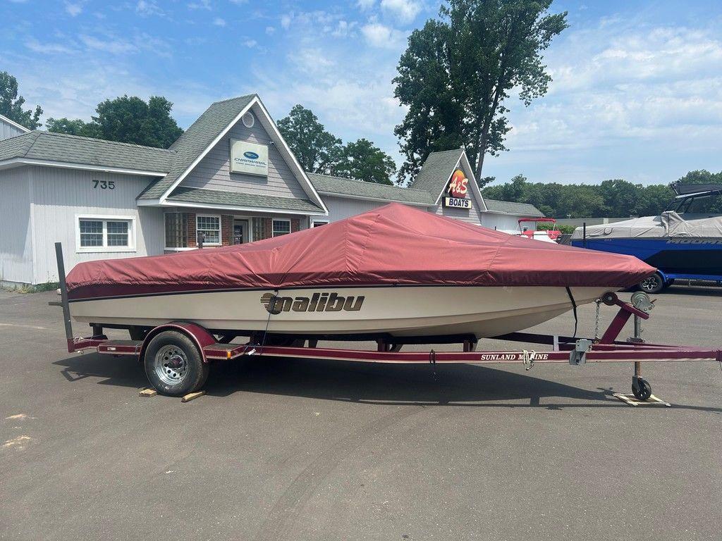 1999 Malibu Sunsetter VLX boat with cover on trailer, parked outside a building.