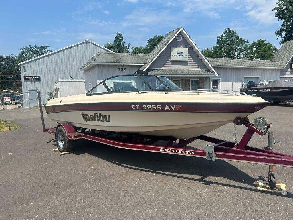 1999 Malibu Sunsetter VLX boat on trailer, parked outside a marine dealership.