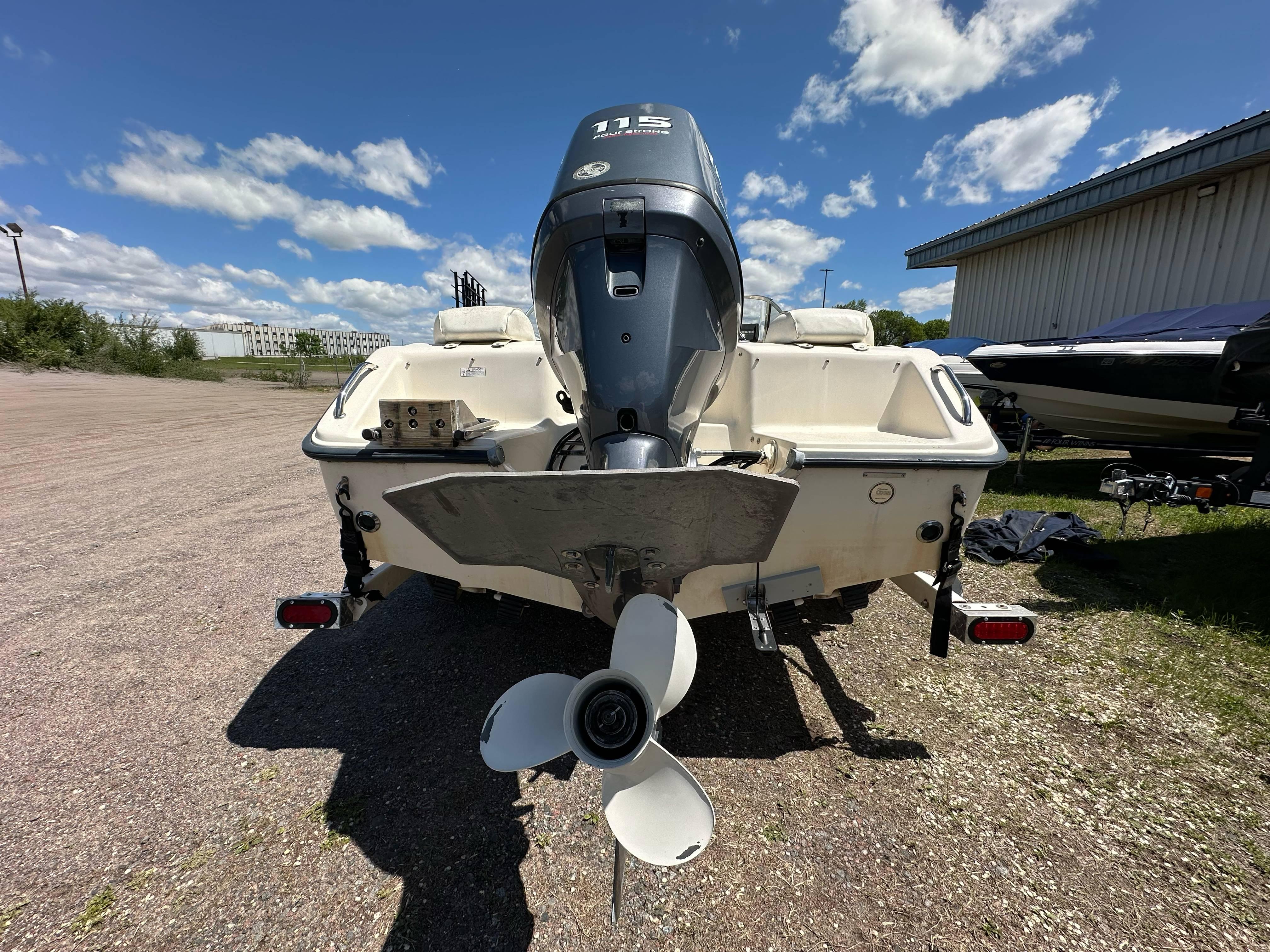 2003 Sea Hunt Escape 186 boat with outboard motor, parked on gravel under a blue sky.