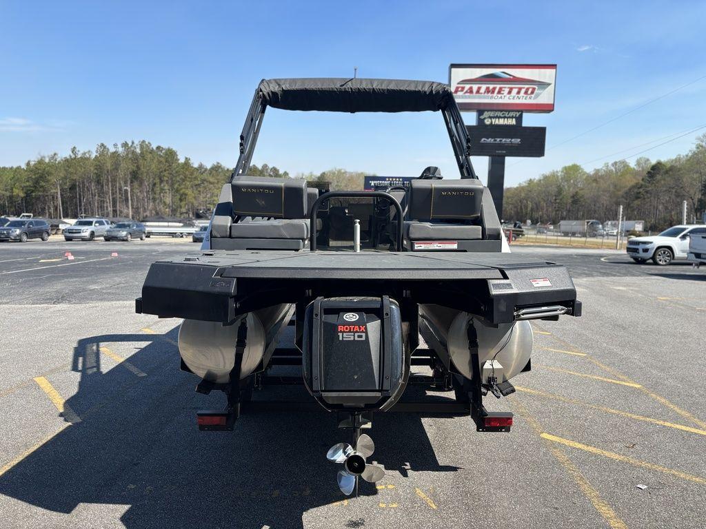 2023 Manitou Explore 22 Max Bench pontoon boat with Rotax 150 engine, parked outdoors.