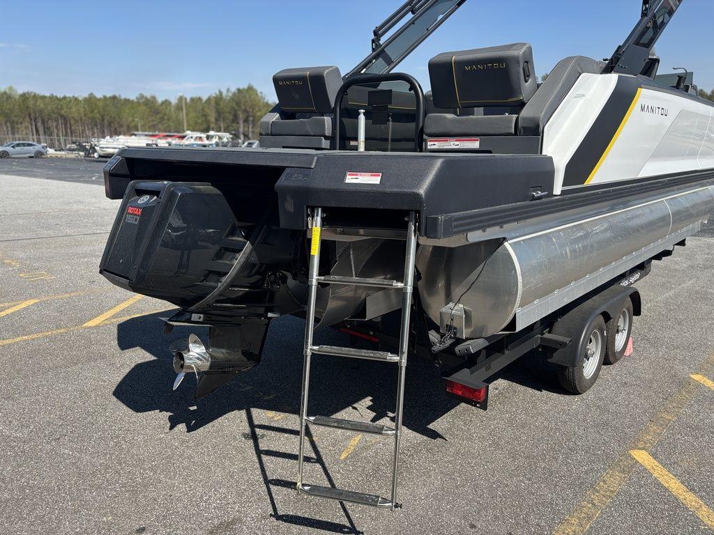 2023 Manitou Explore 22 Max Bench pontoon boat with ladder and motor, parked on trailer.