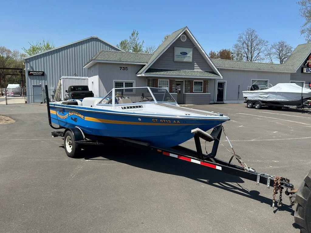 1980 Ski Supreme boat on trailer in parking lot, near gray building.