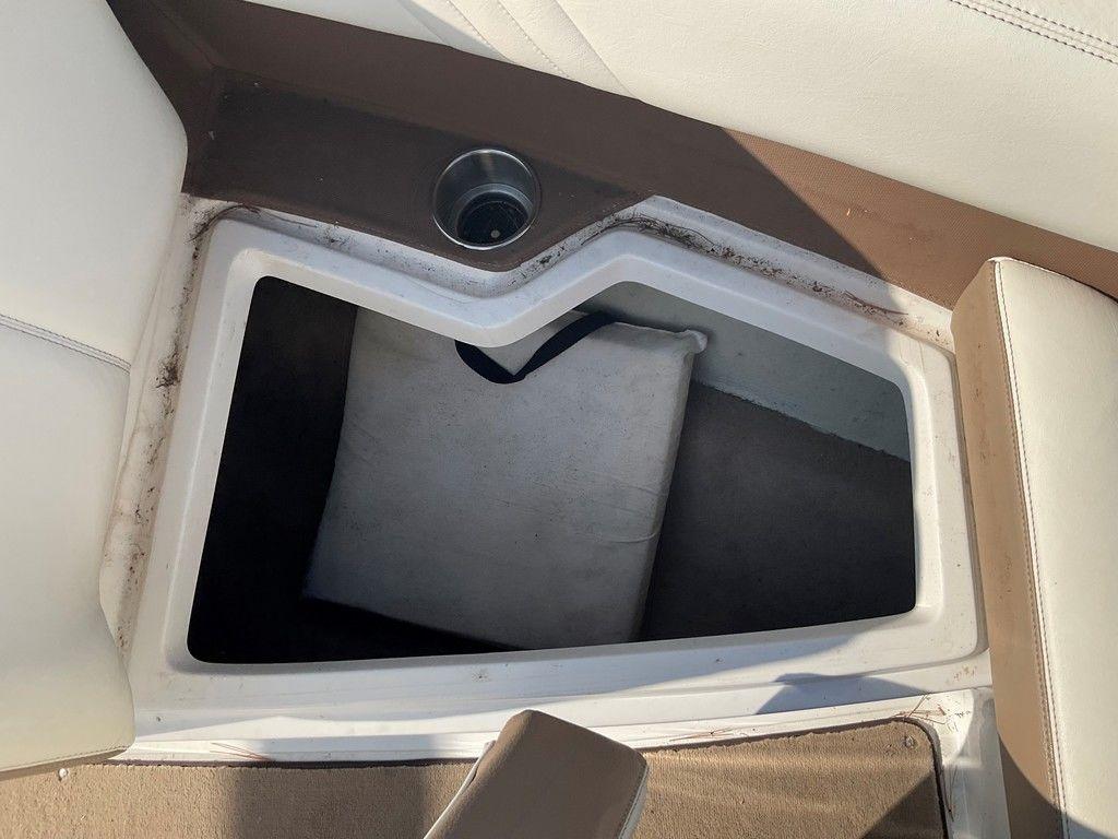 Storage compartment in a 2013 Cobalt 210 boat with cup holder and cushion.