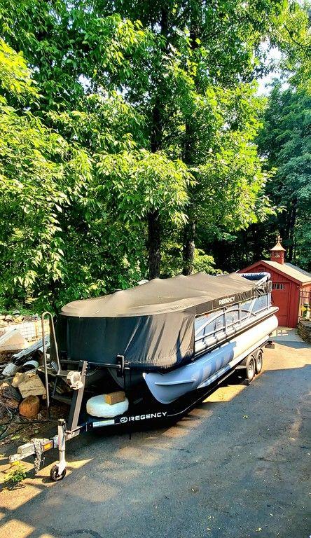 2017 Regency 220 DL3 pontoon boat covered, parked on a driveway near trees.