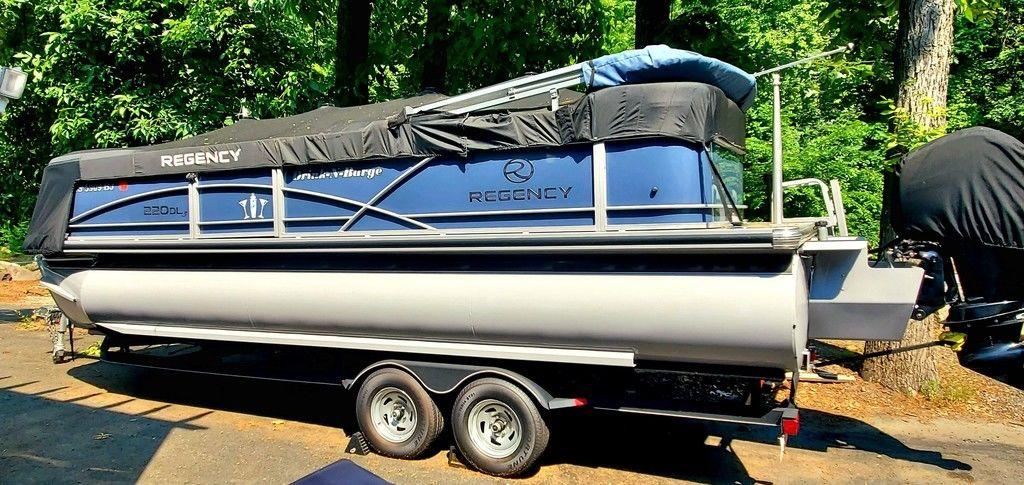2017 Regency 220 DL3 pontoon boat on trailer, covered, parked in wooded area.