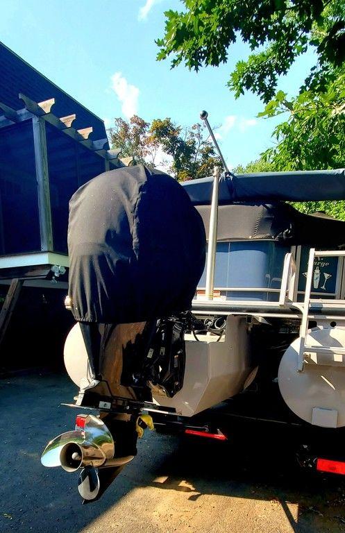 2017 Regency 220 DL3 pontoon boat with covered outboard motor, parked under trees.
