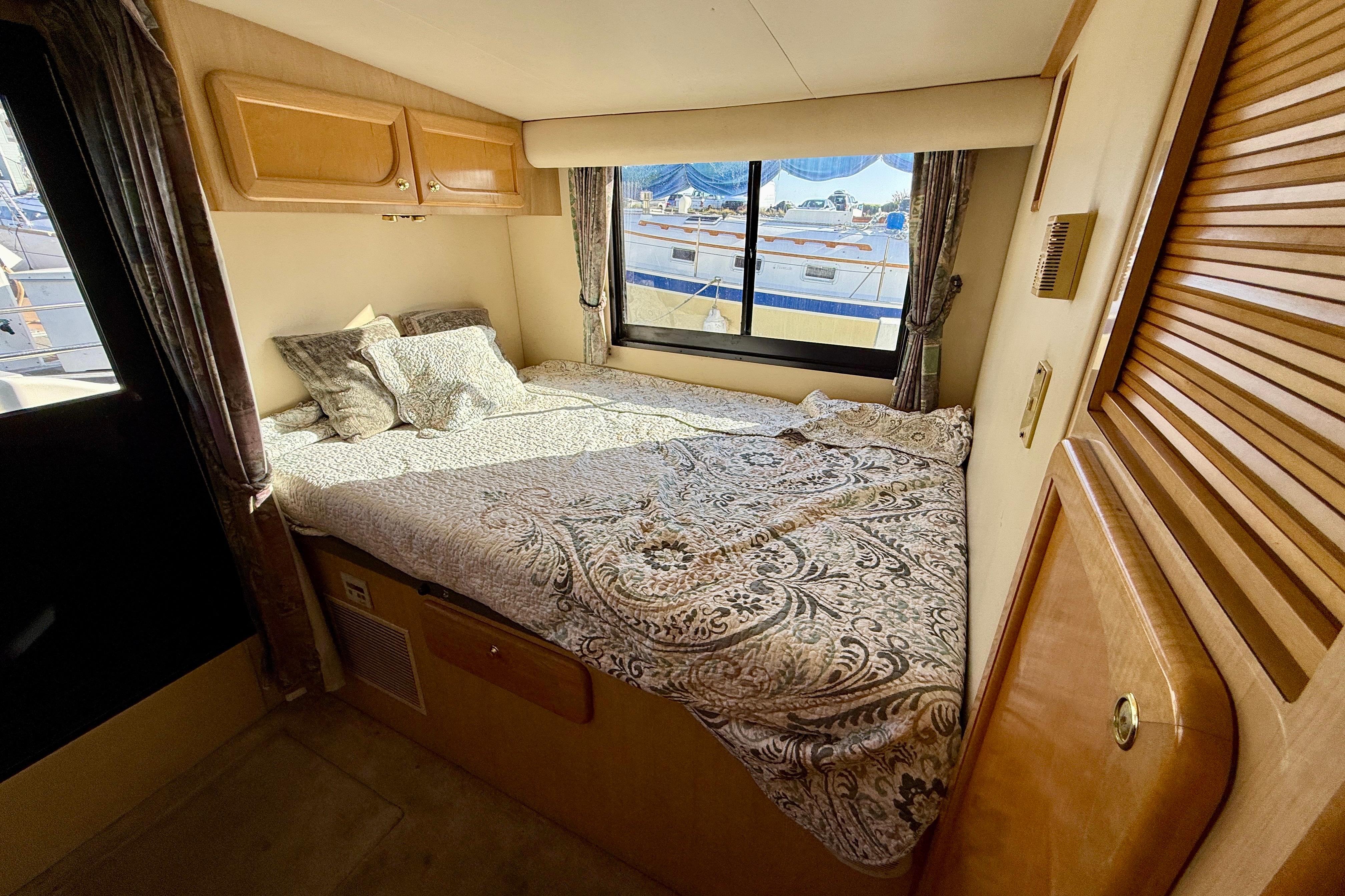 Cozy bedroom interior of 1999 Bluewater 5800 yacht with patterned bedding and window view.