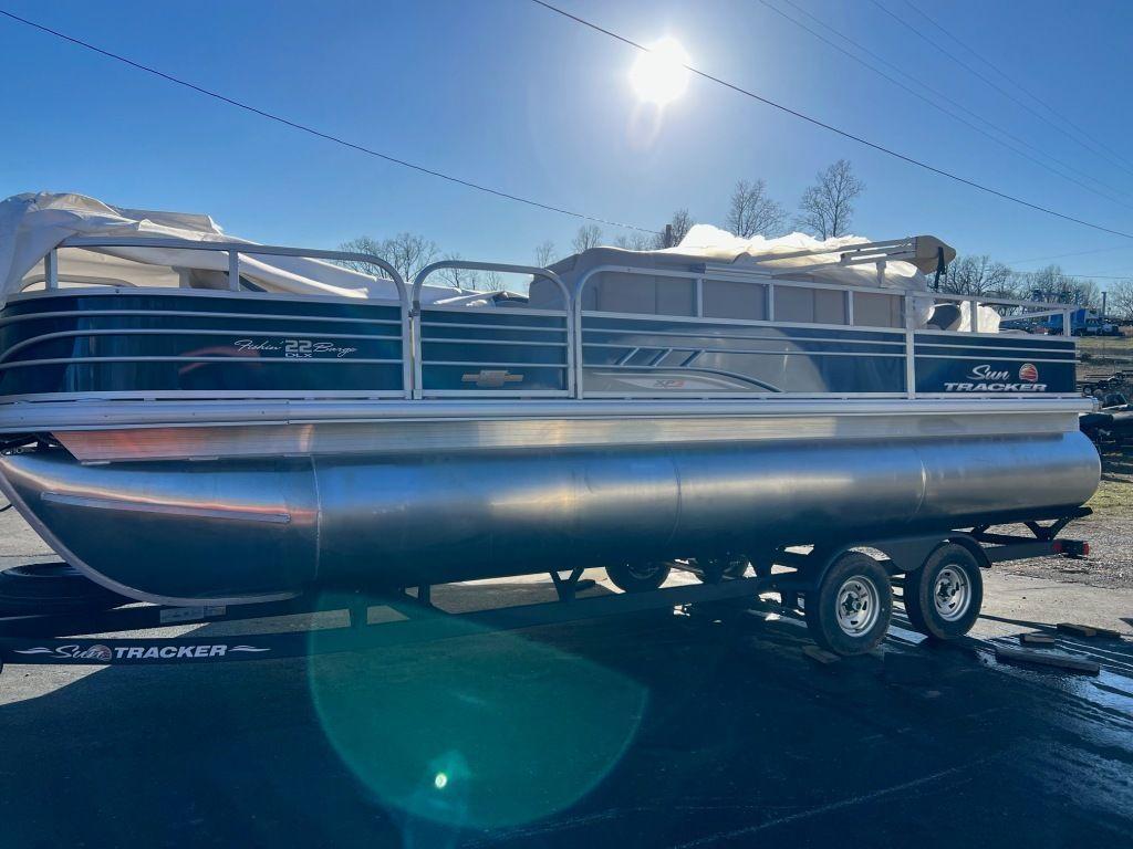 2023 Sun Tracker FISHIN' BARGE® 22 XP3 pontoon boat on trailer under bright sun.