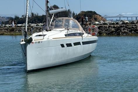 2021 Jeanneau Sun Odyssey 349 sailboat navigating calm waters near a rocky shoreline.