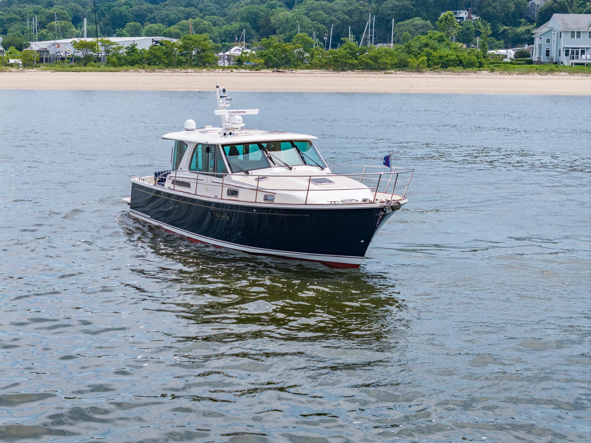 2024 Sabre 43 Salon Express yacht cruising on calm waters near a sandy shoreline.