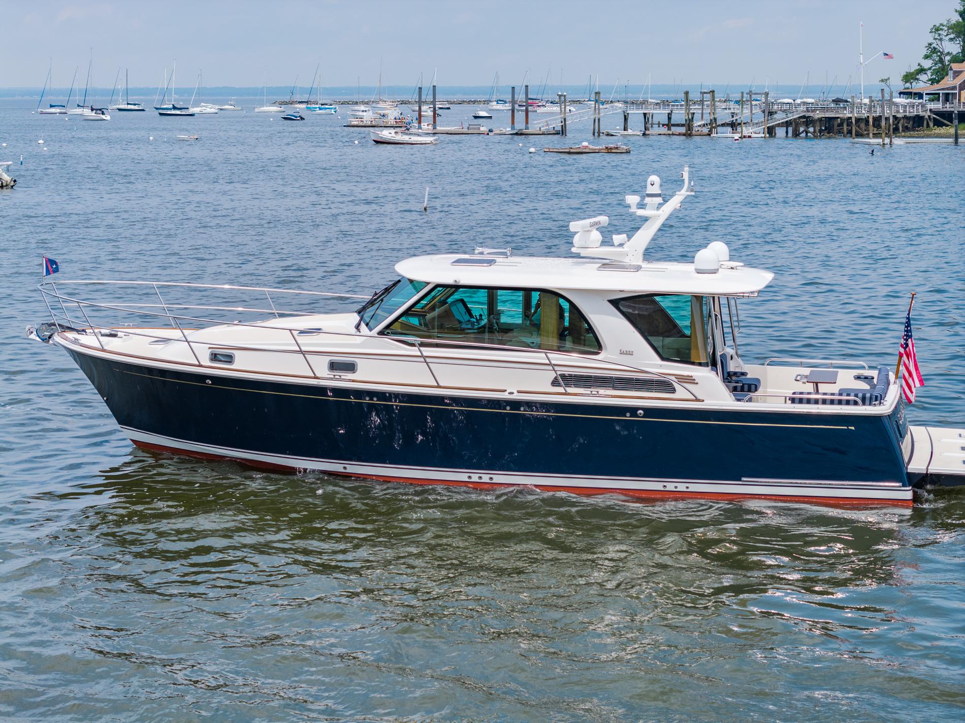 2024 Sabre 43 Salon Express yacht on calm waters, docked with scenic marina background.