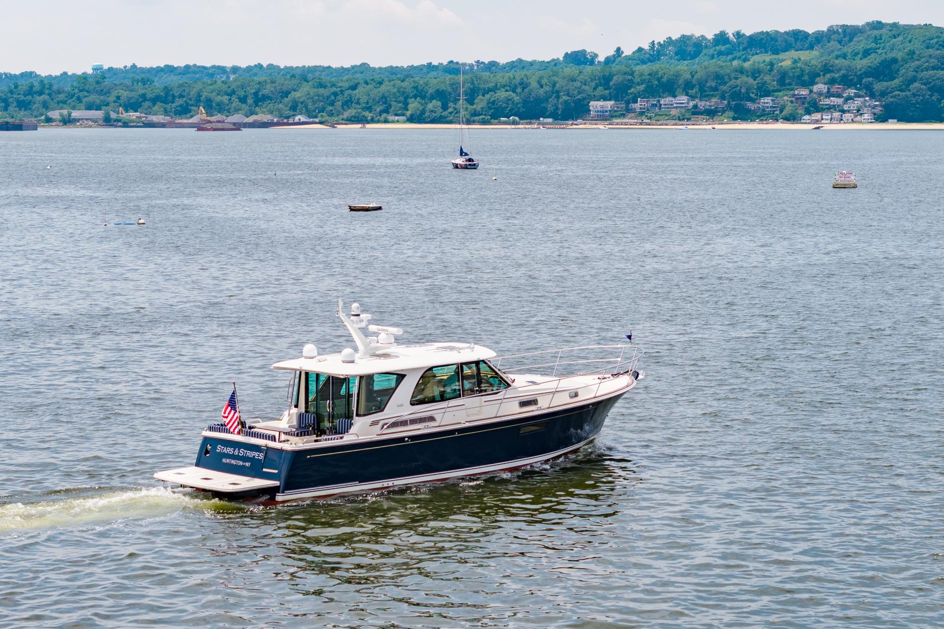 2024 Sabre 43 Salon Express cruising on a scenic lake with lush green shoreline.