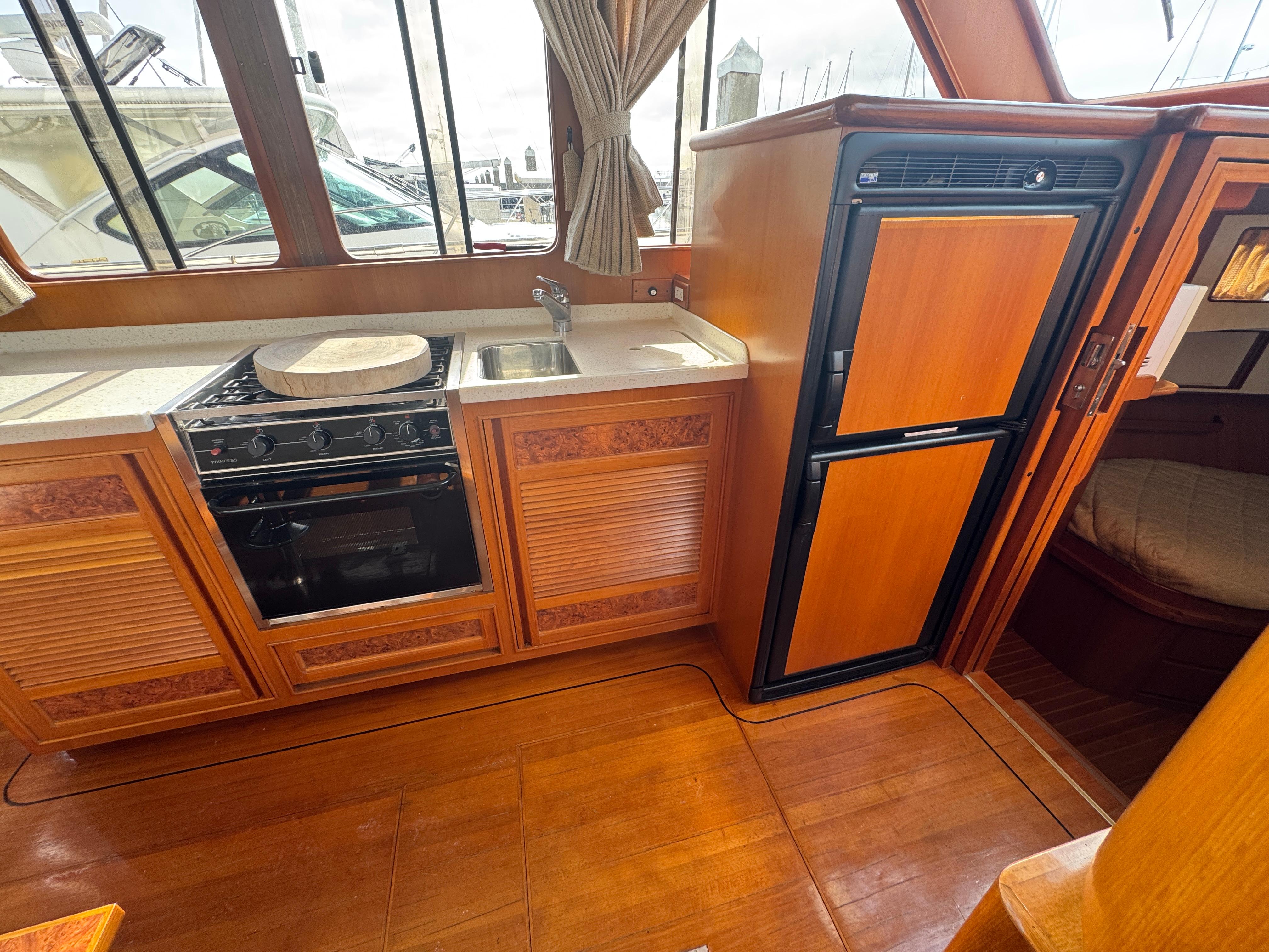2003 President Performance Trawler kitchen with stove, sink, and refrigerator, featuring wood cabinetry.