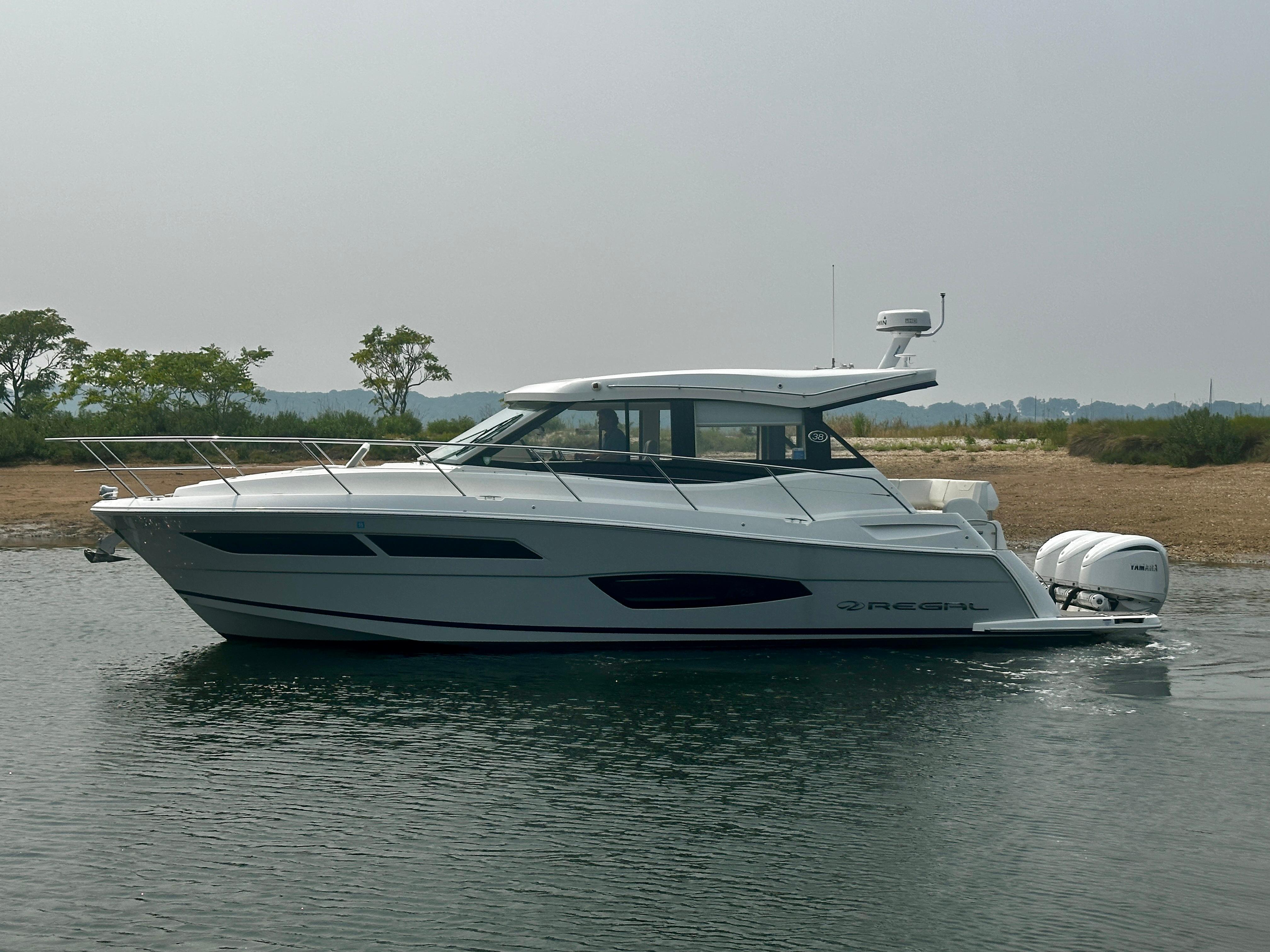 2022 Regal 38 XO boat on calm water, side view with trees in the background.