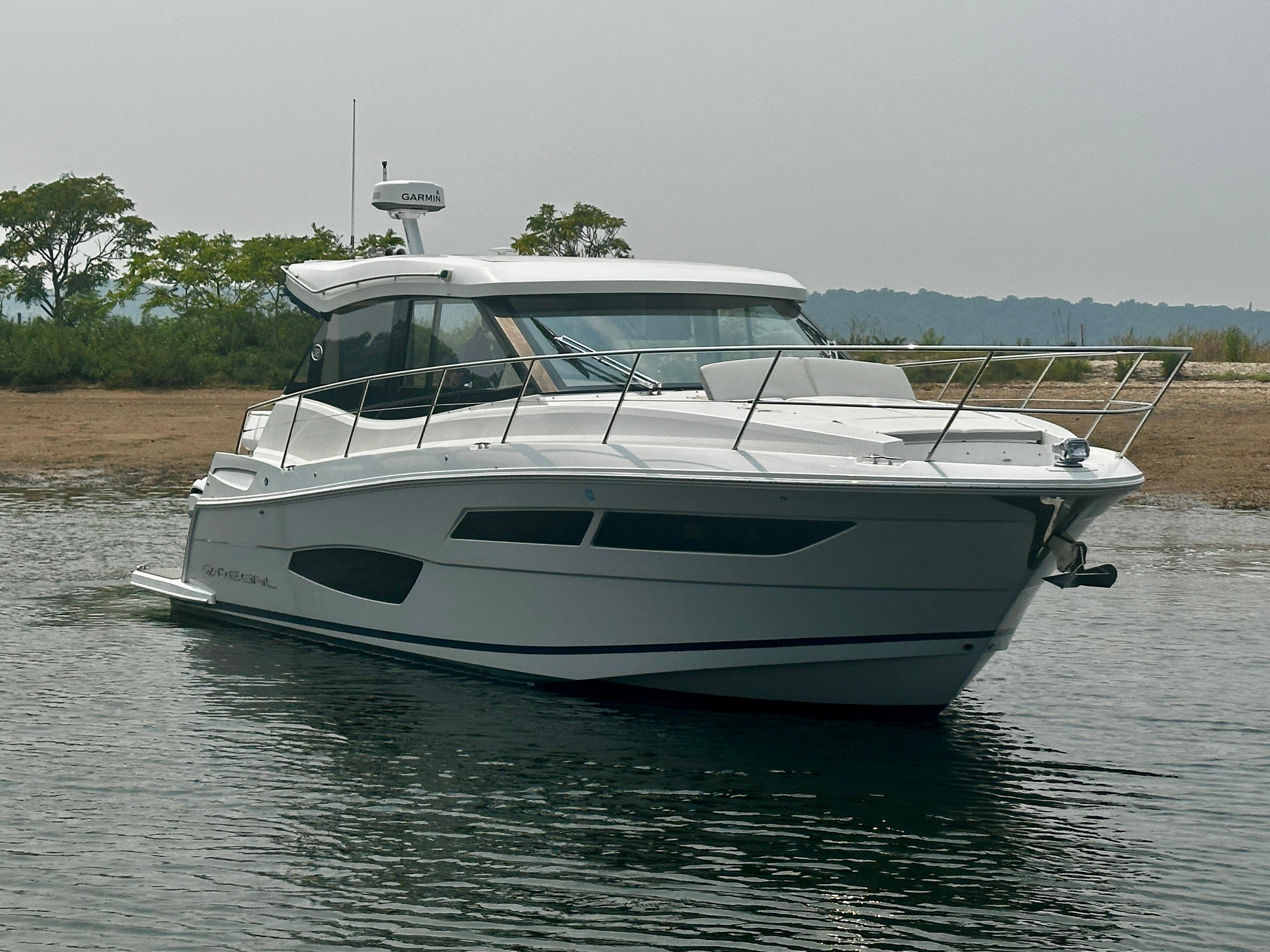 2022 Regal 38 XO boat on calm water near a grassy shoreline.
