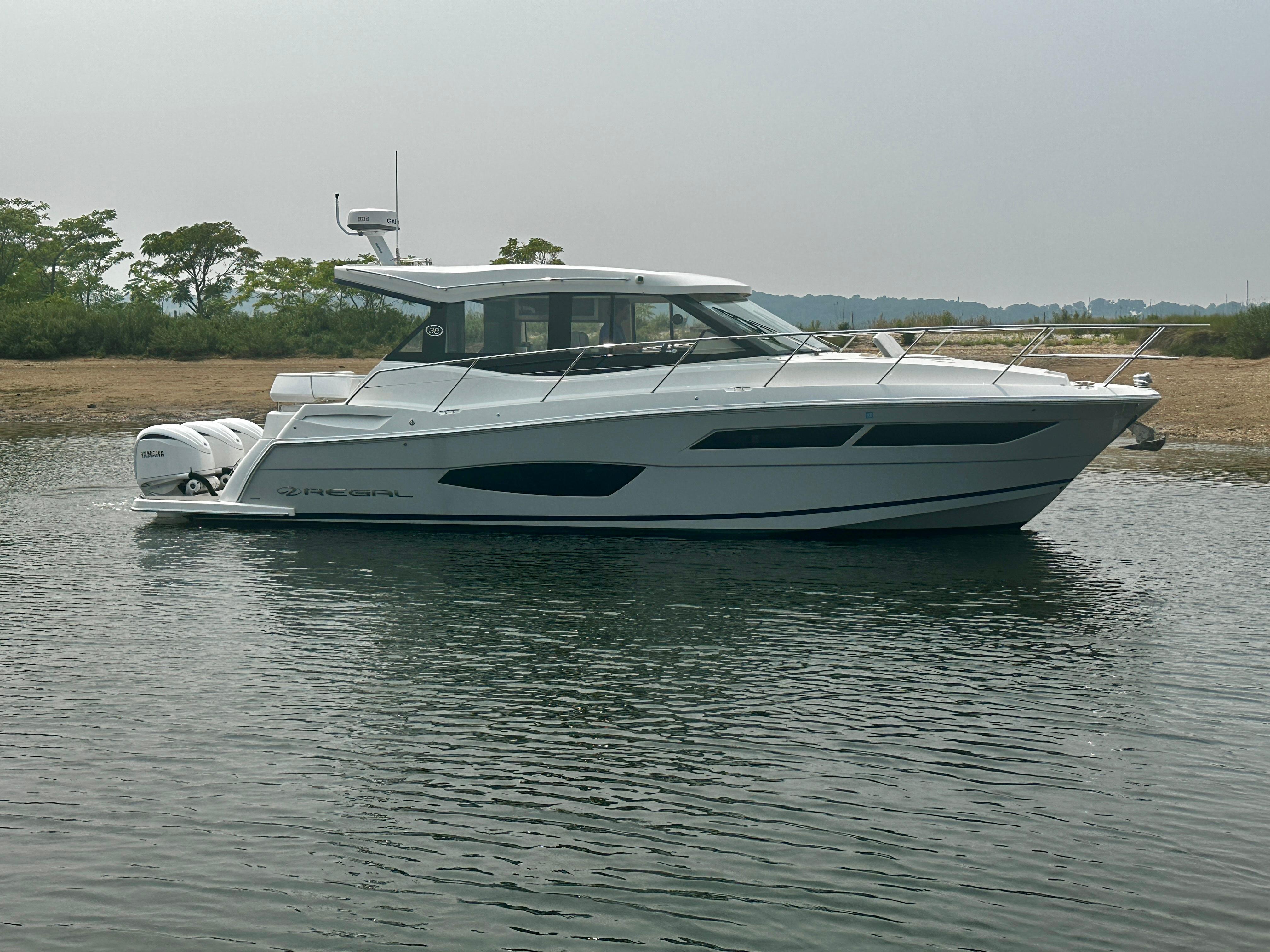 2022 Regal 38 XO boat on calm water near a sandy shore.