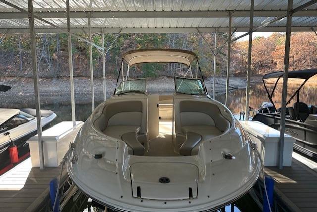 2002 Sea Ray 240 Sundeck boat docked under a covered marina with autumn trees in the background.