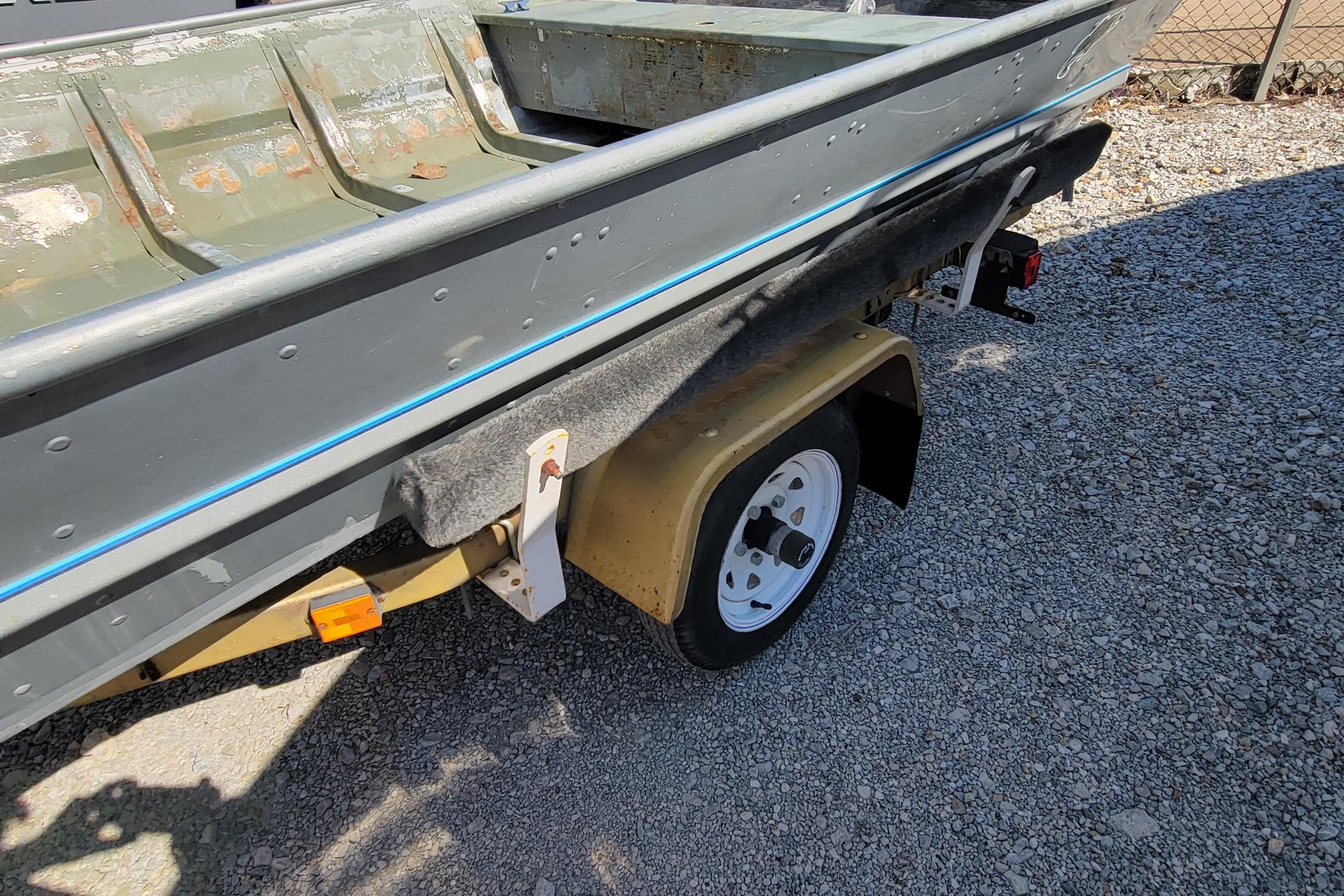 1973 Monark 14 Jon boat on trailer, showing weathered interior and gravel ground.