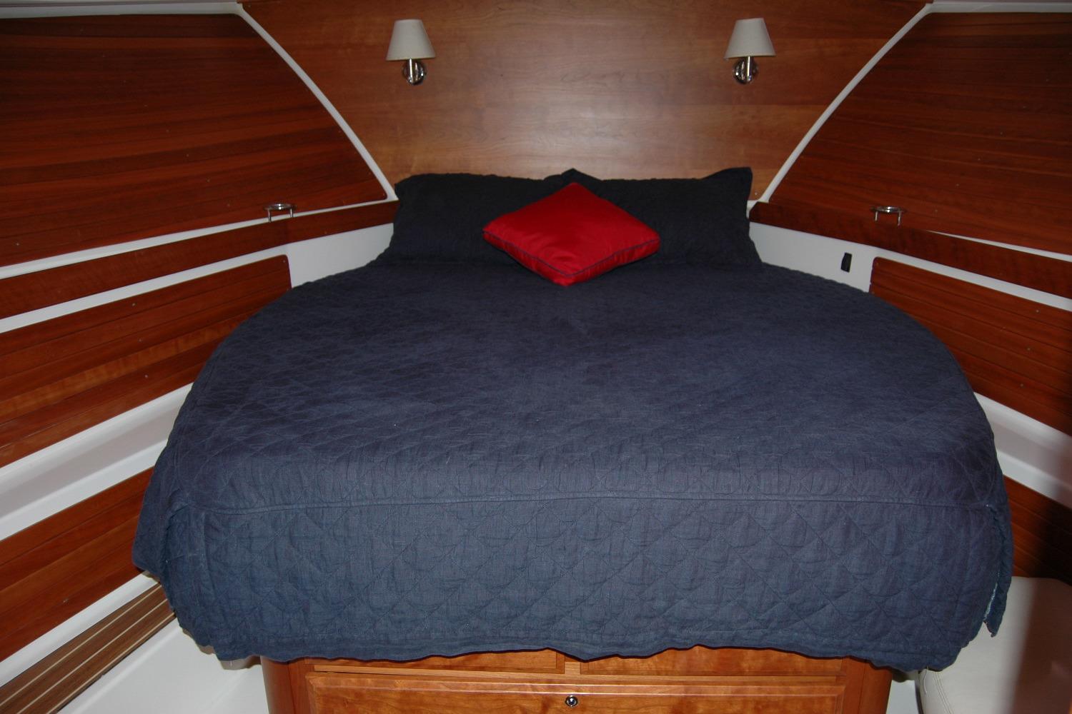 Cozy cabin bedroom in 2015 Back Cove 37 yacht with blue bedding and red pillow.