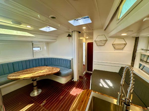 Interior of 1983 Tayana 55 yacht with modern seating, wooden table, and sleek kitchen area.