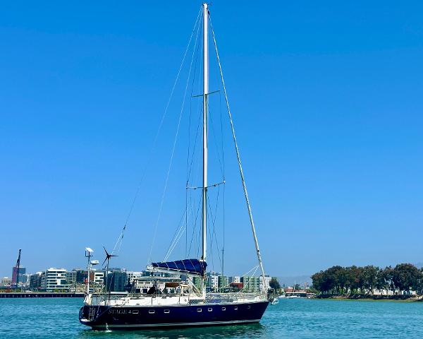 Sailing yacht Tayana 55, 1983 model, on calm waters with cityscape background.