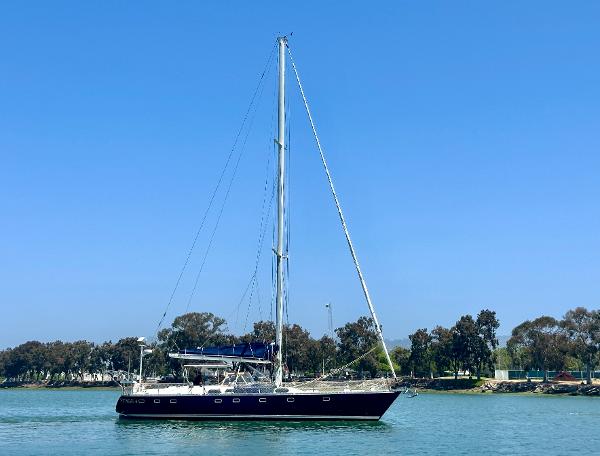 1983 Tayana 55 sailboat on calm water with clear blue sky background.