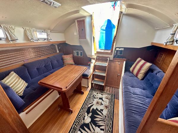 1986 Nonsuch Ultra yacht interior with blue seating, wooden table, and floral rug.