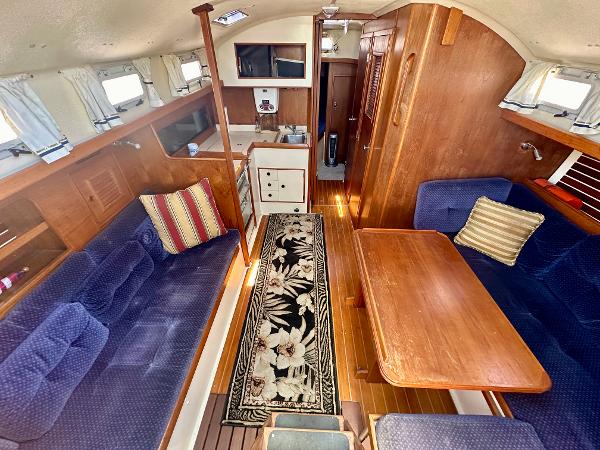 1986 Nonsuch Ultra yacht interior with blue seating, wooden table, and floral rug.