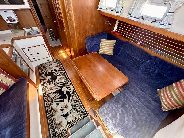 Cozy 1986 Nonsuch Ultra yacht interior with blue seating, wooden table, and floral rug.