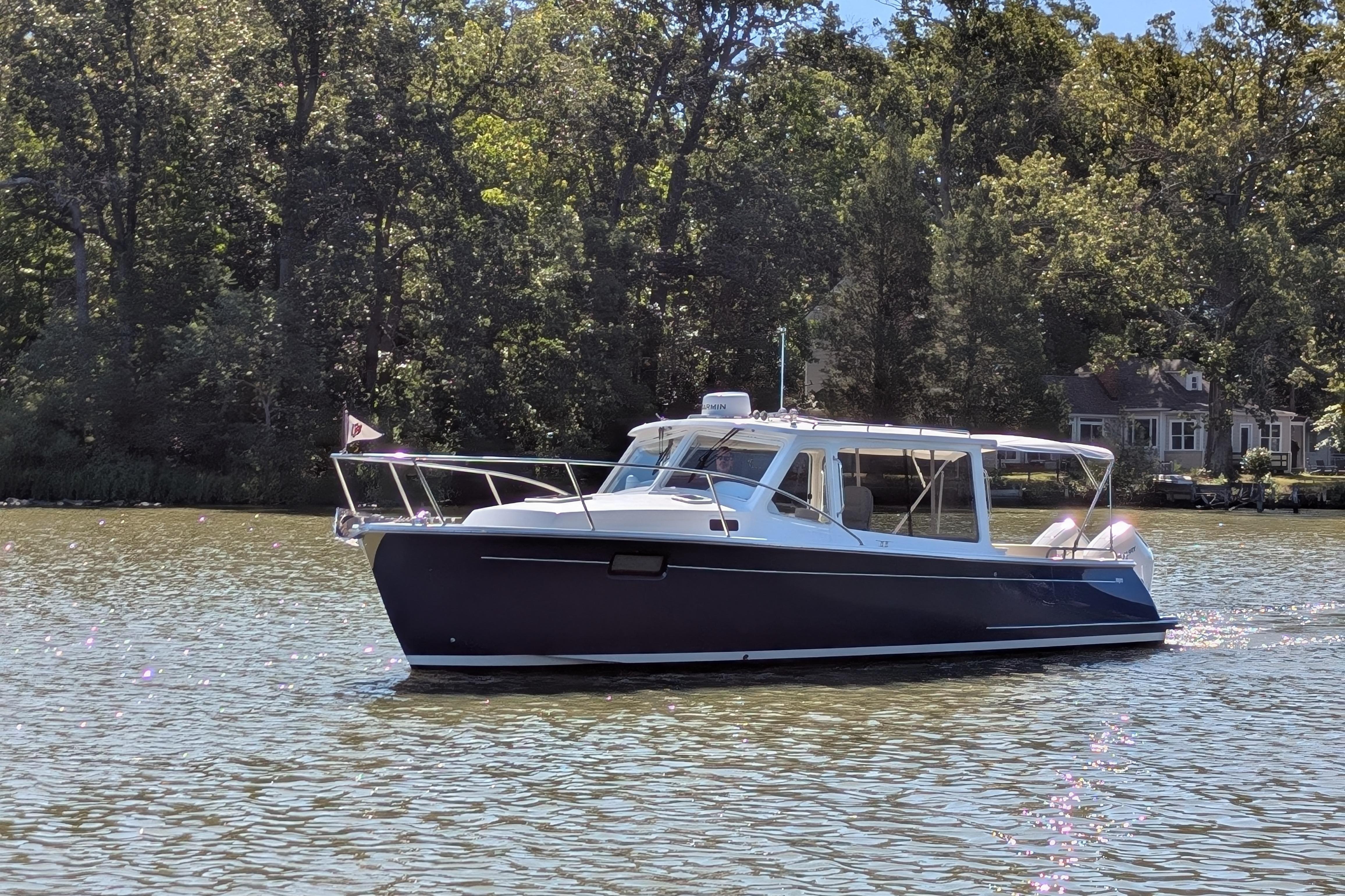 2024 MJM 35 boat on a serene lake with lush green trees in the background.