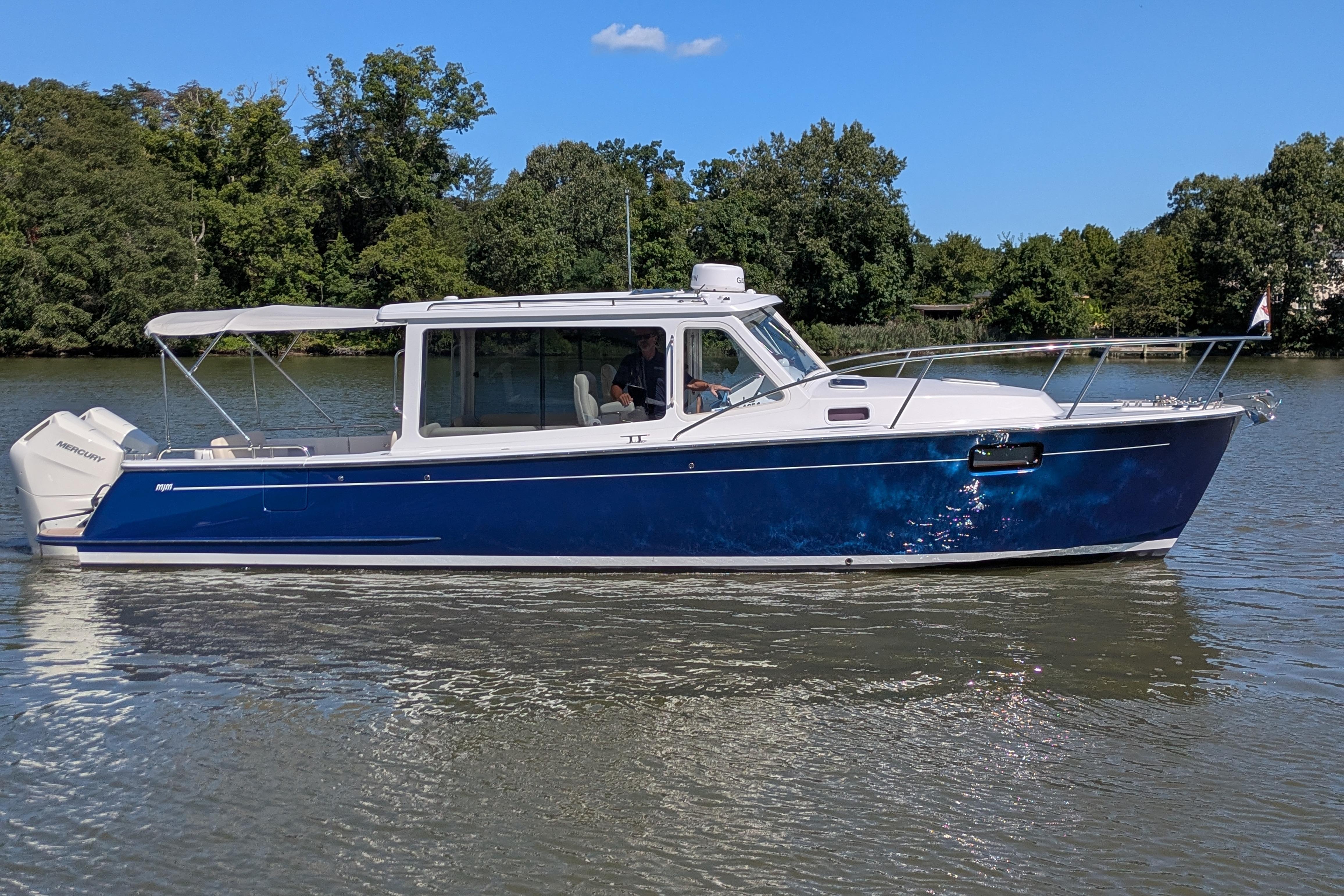 2024 MJM 35 boat on a calm river with lush green trees.