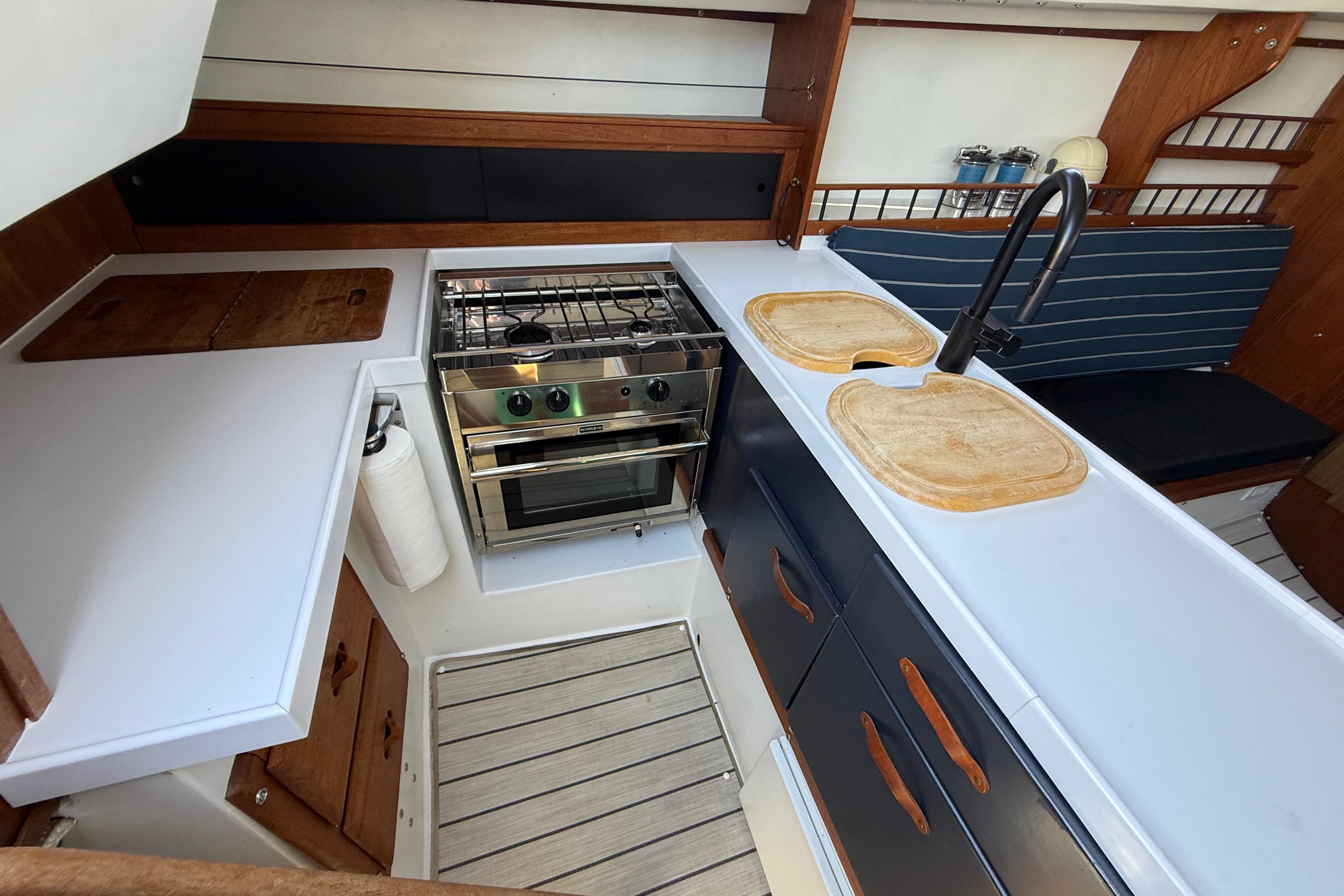 Interior of 1981 Catalina 30 sailboat kitchen with stove, sink, and wooden cabinetry.