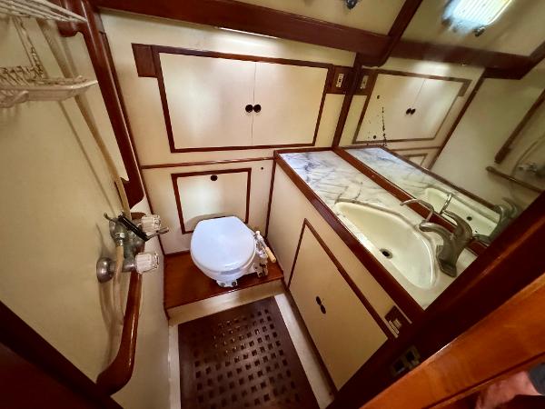 1983 Tayana 52 Aft Cockpit yacht bathroom with sink, toilet, and wooden cabinetry.