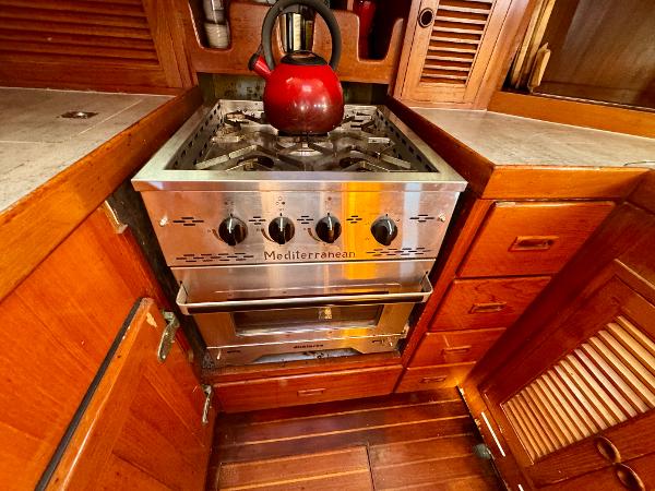 Stainless steel stove with red kettle in 1983 Tayana 52 Aft Cockpit yacht kitchen.