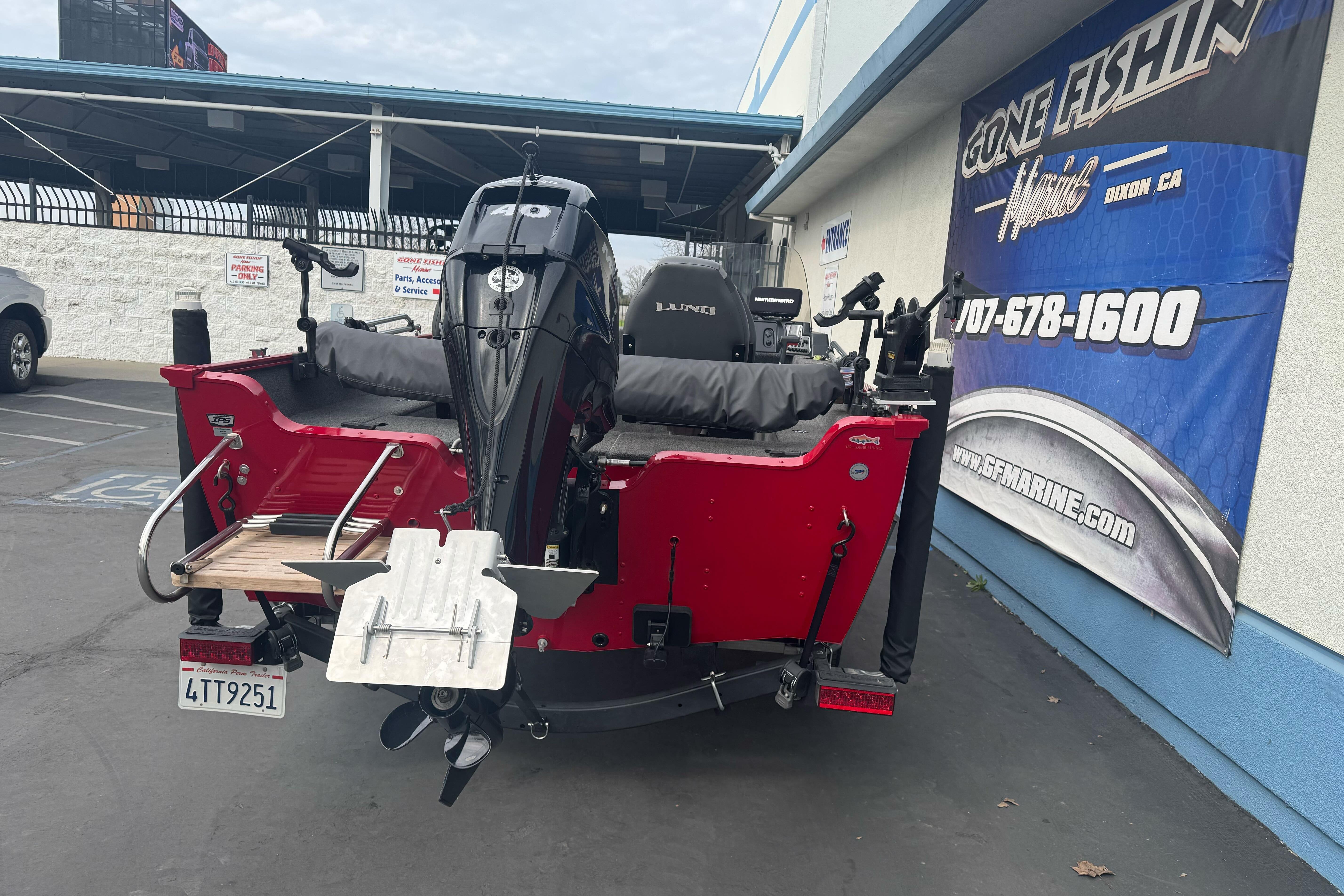 2021 Lund 1650 Angler SS boat with motor, parked near a marine store.