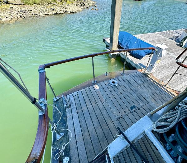 1966 Rampart 48 boat docked, featuring wooden deck and railing, moored by a pier.