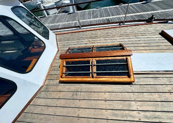 Wooden deck of 1966 Rampart 48 boat with a skylight and dock view.