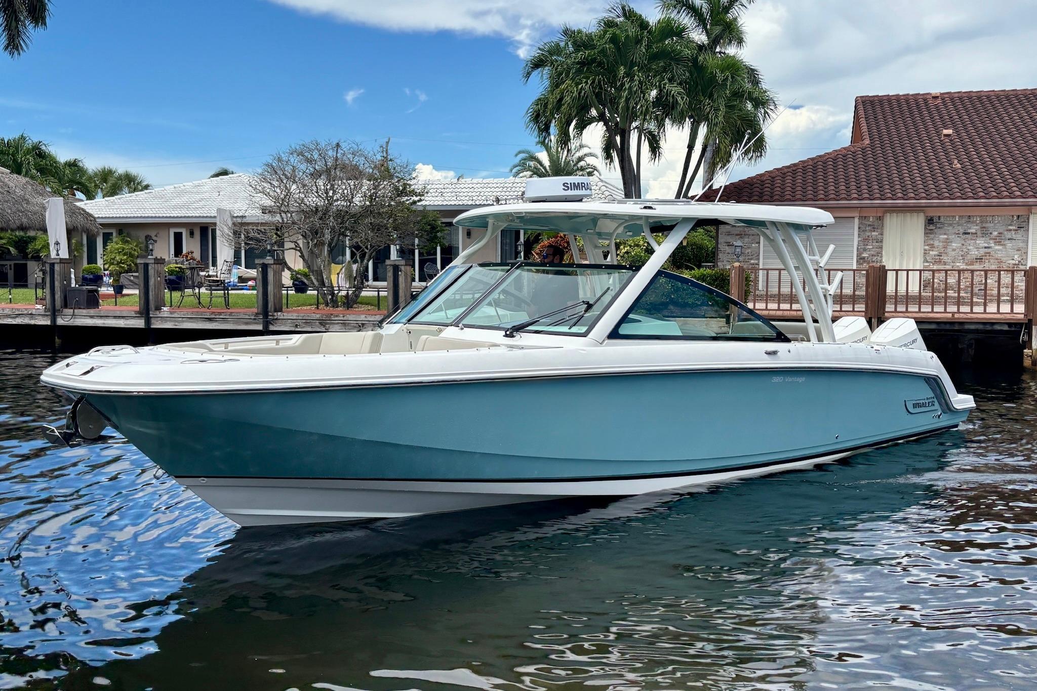 2024 Boston Whaler 320 Vantage boat docked near waterfront homes, under a clear sky.