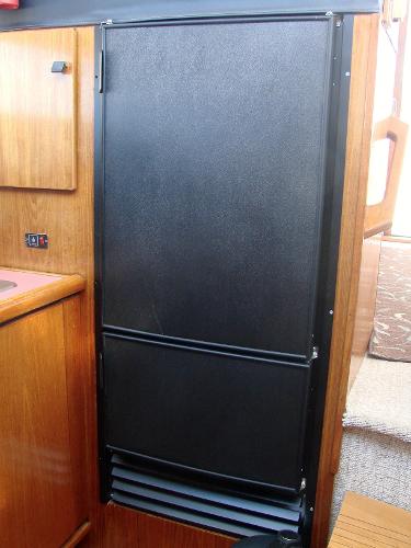 1987 Bayliner 3888 Motoryacht interior with black refrigerator and wooden cabinetry.