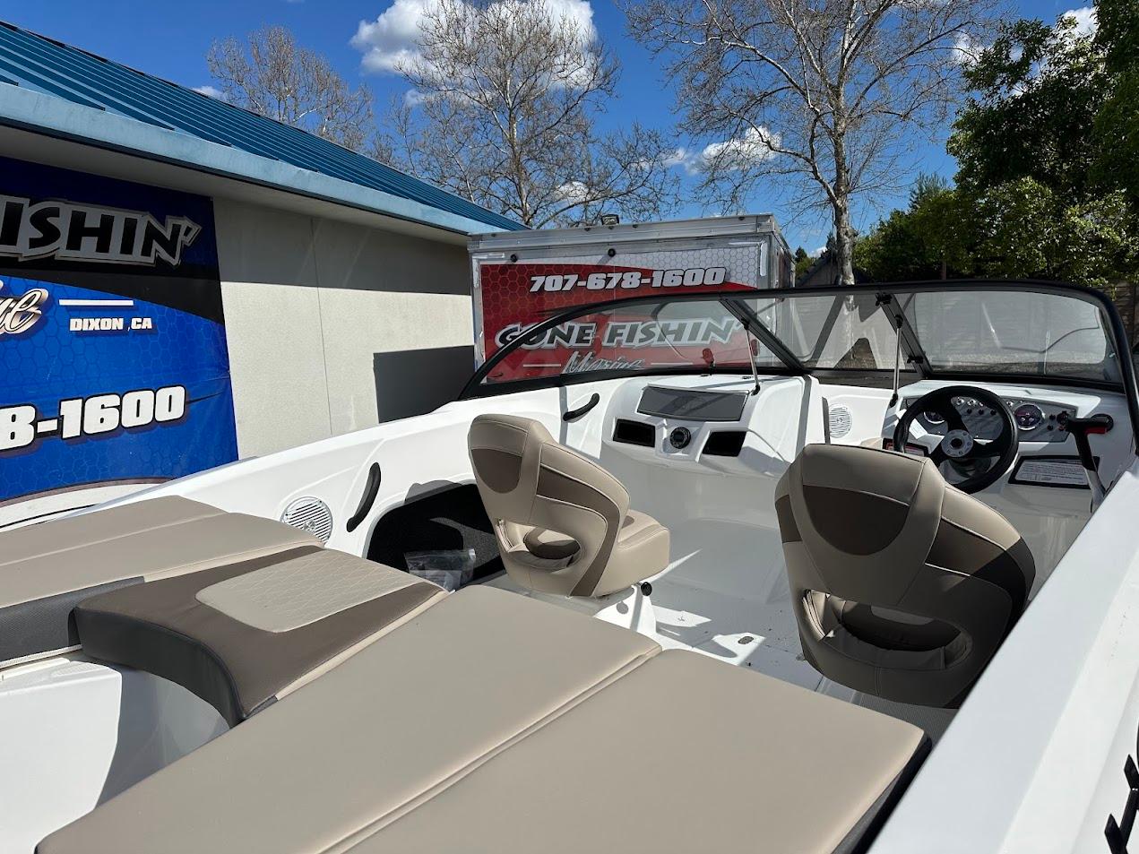 2025 Tahoe 185 S boat interior with beige seating, parked near a building under a blue sky.