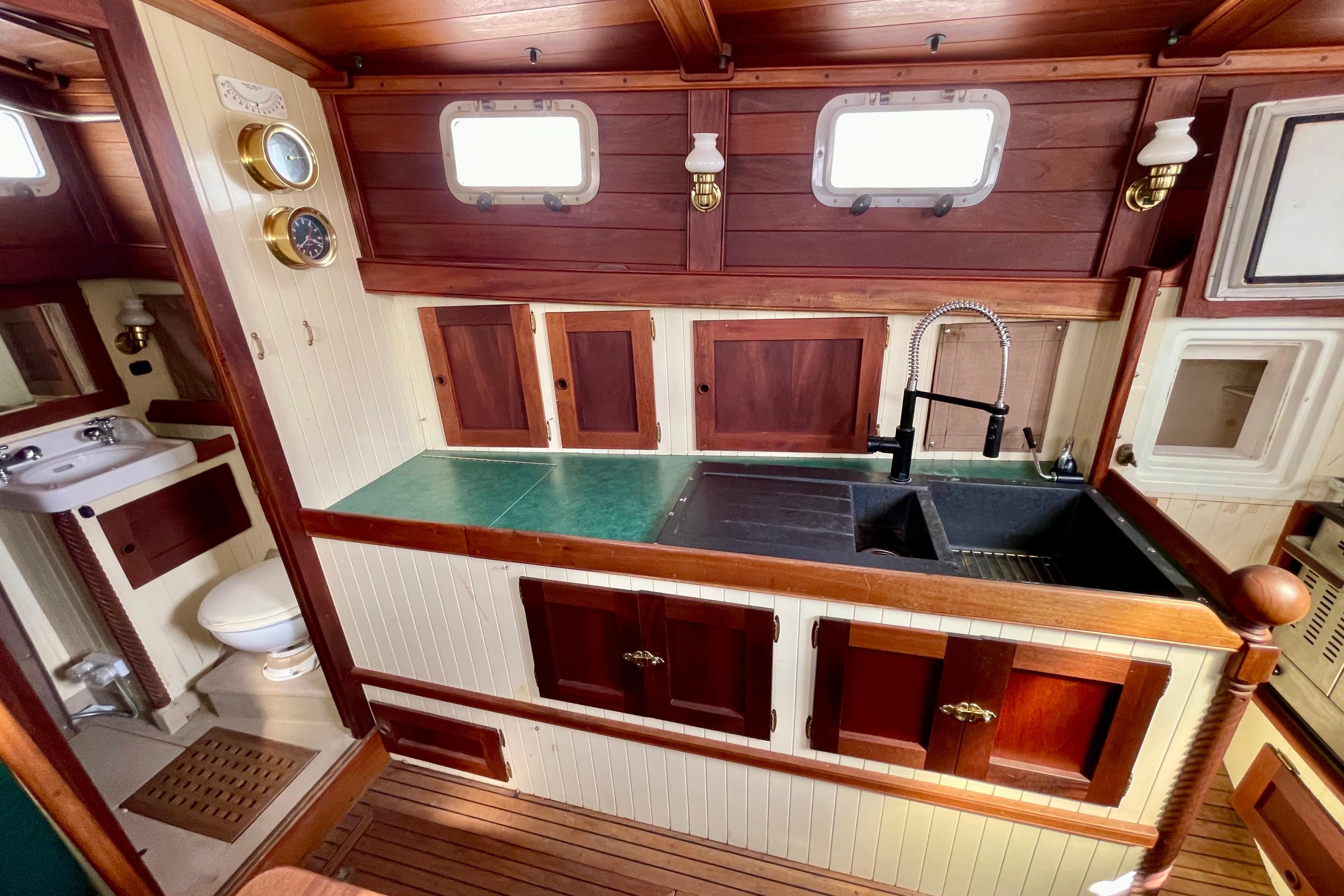 Wooden boat interior with vintage kitchen and bathroom, featuring brass fixtures and porthole windows.