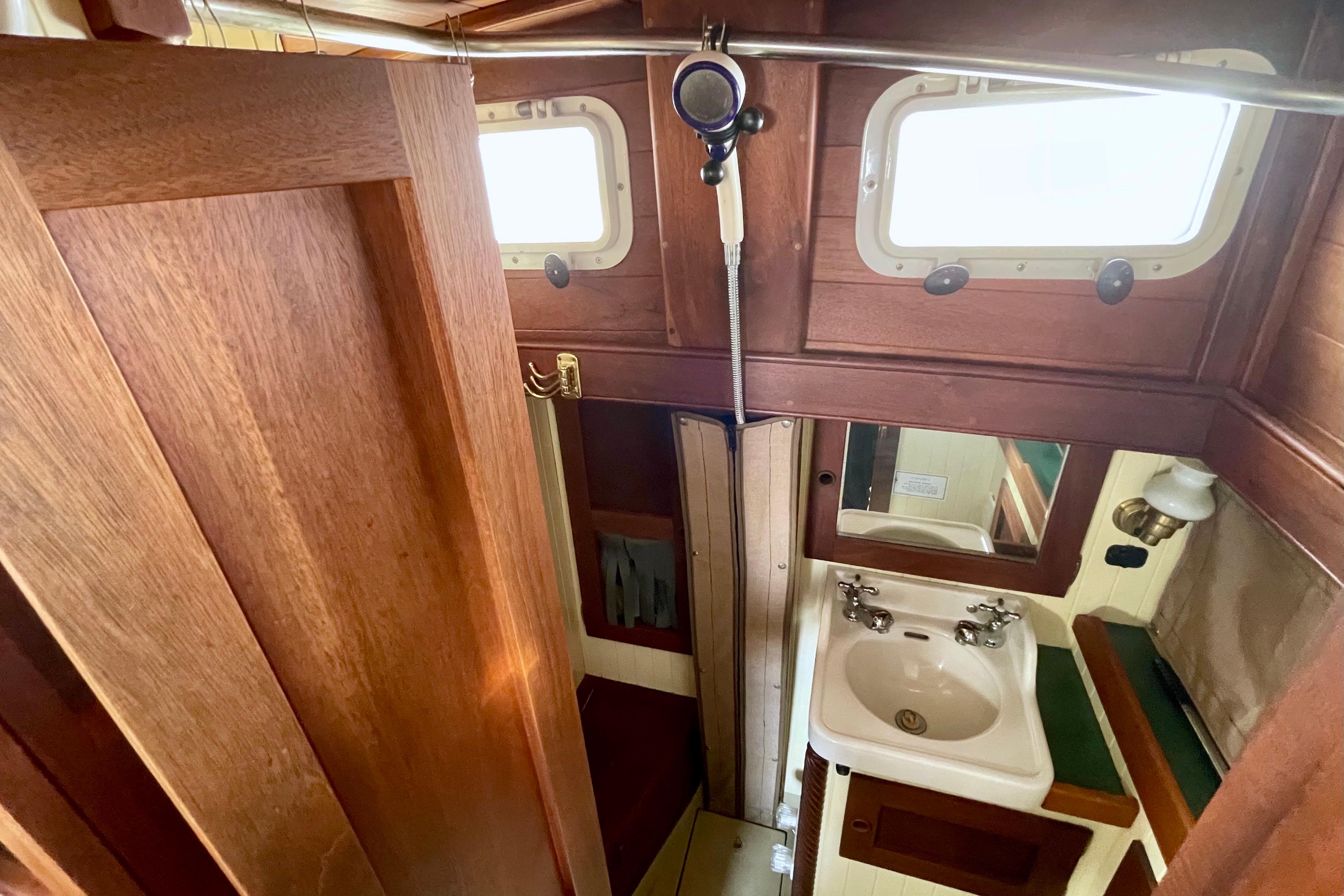 Compact wooden boat bathroom with sink, mirror, and shower in 2008 Pinky Custom model.