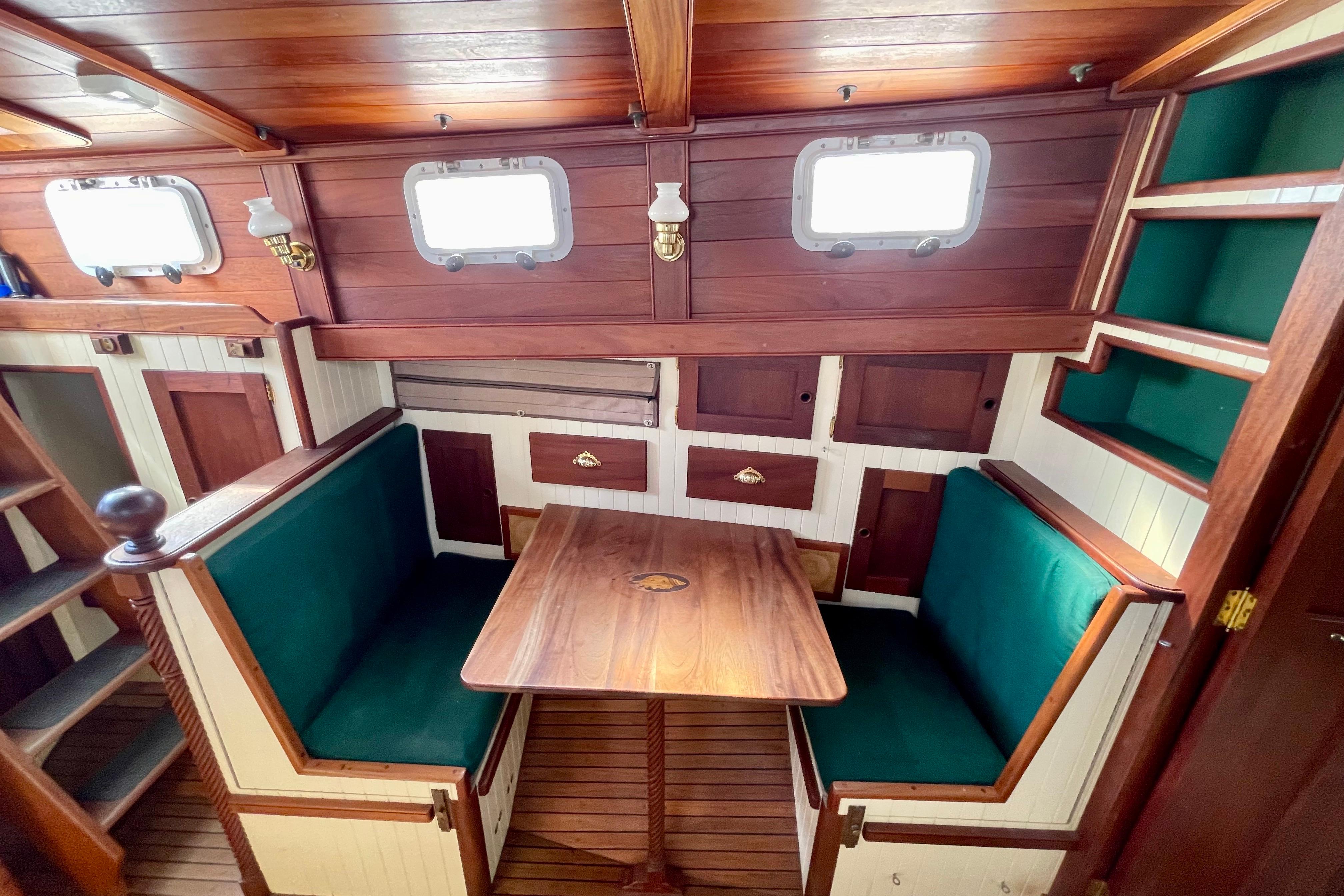 Cozy wooden boat interior with green cushioned seating, table, and storage, Pinky Custom 2008 model.