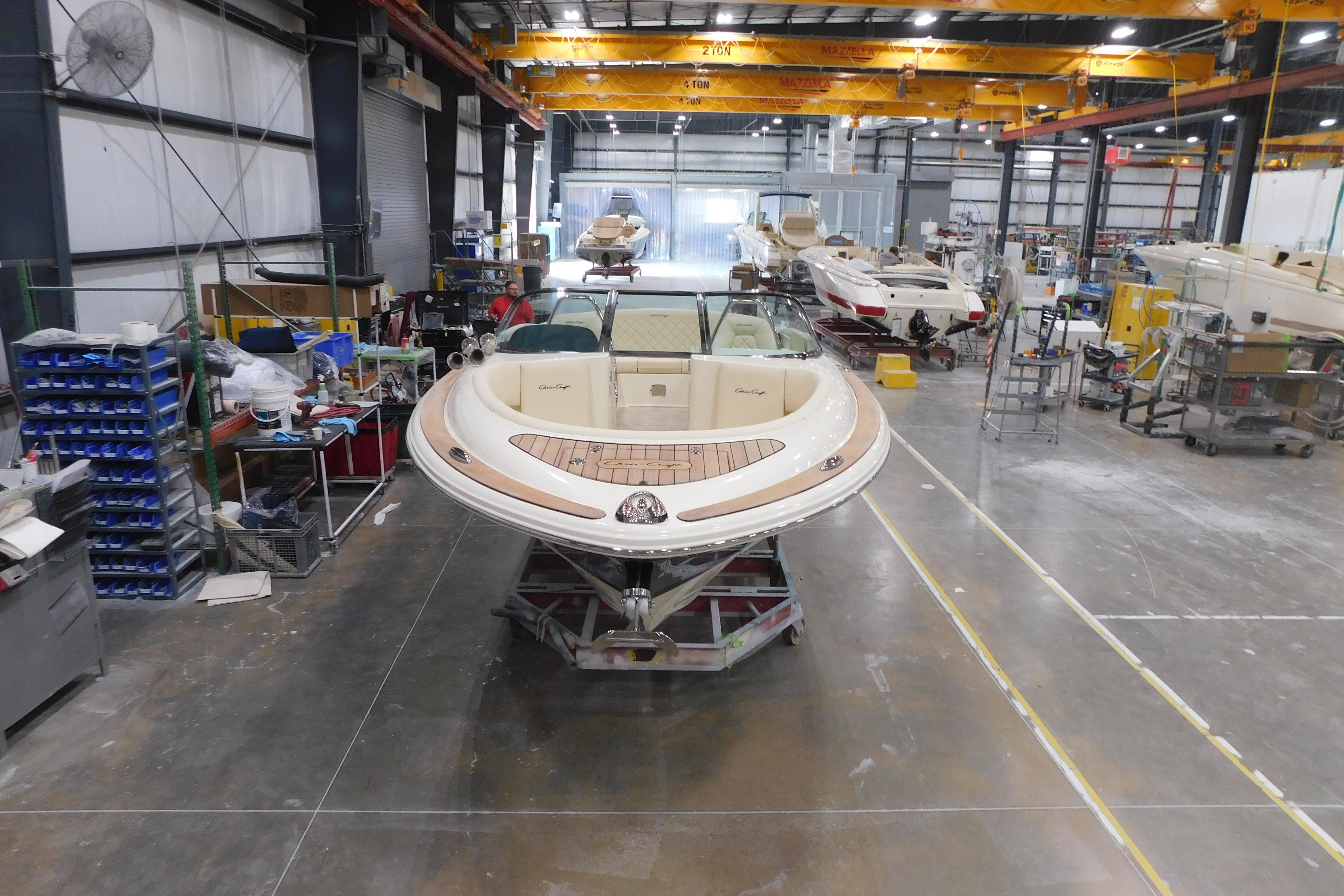 2026 Chris-Craft Launch 27 boat in a manufacturing facility, surrounded by equipment and other boats.