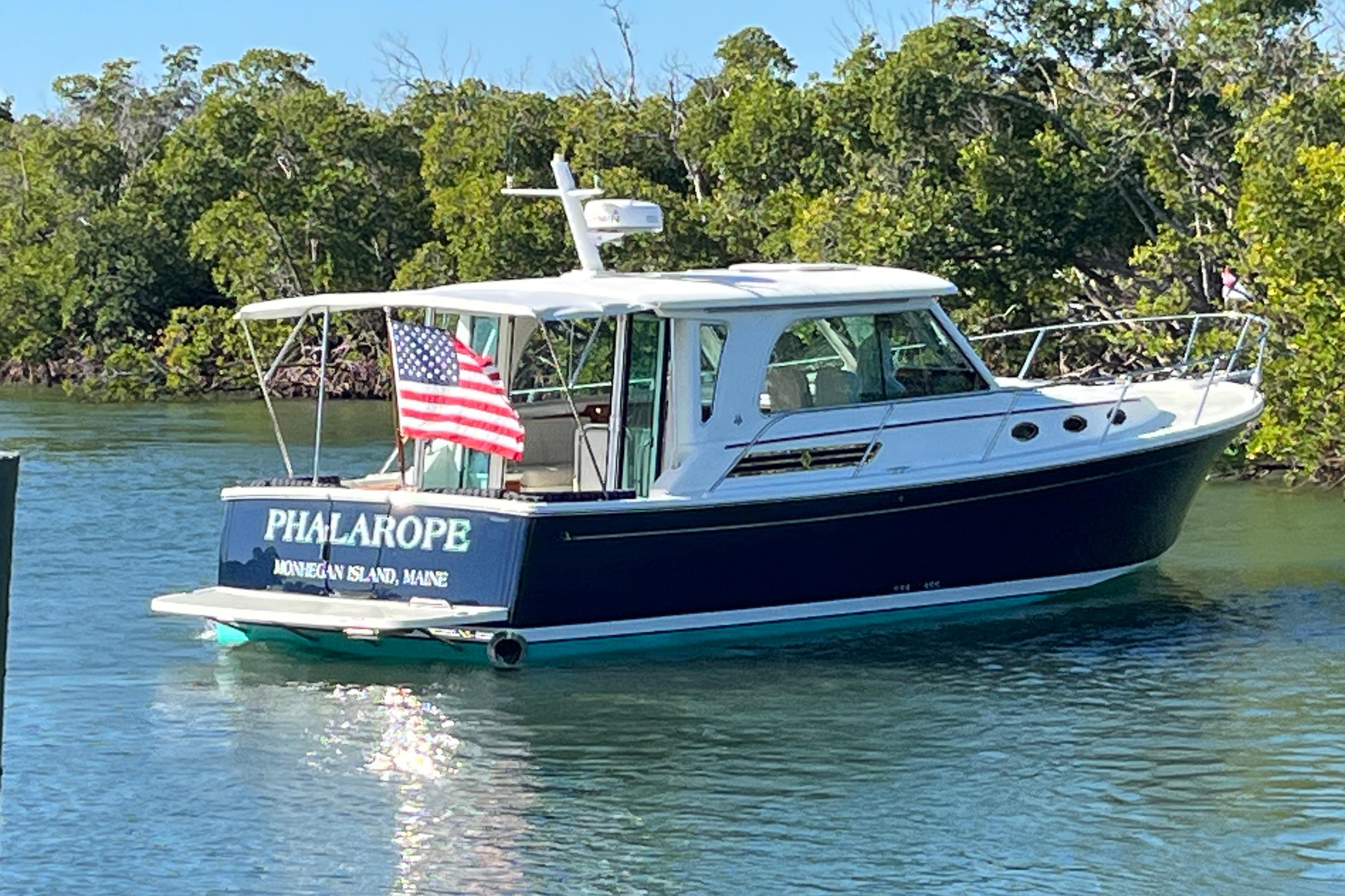 2017 Back Cove 37 boat named u0022Phalaropeu0022 on water, American flag, lush greenery background.