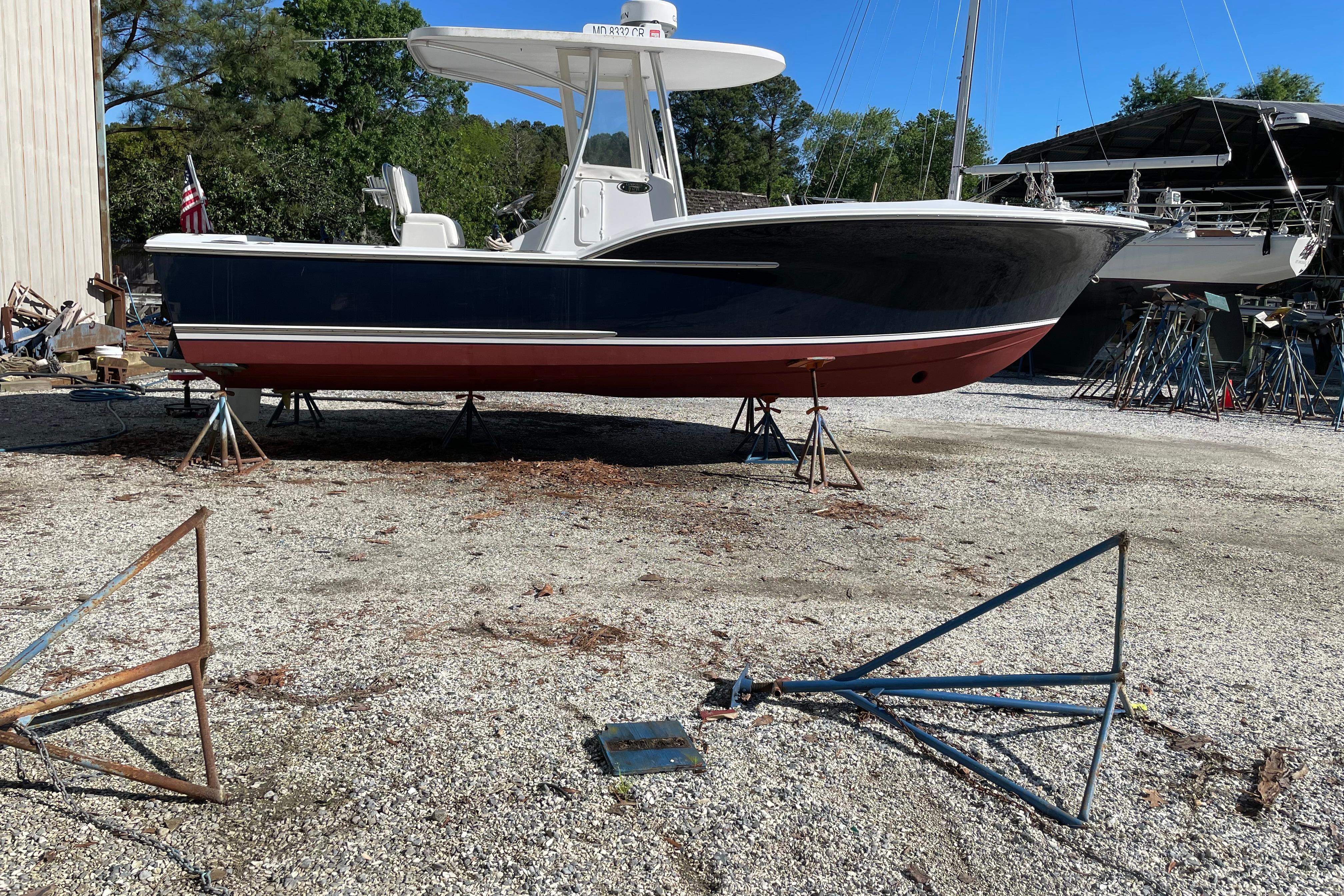 2013 Composite Yacht 26 on stands in a boatyard, surrounded by trees and equipment.