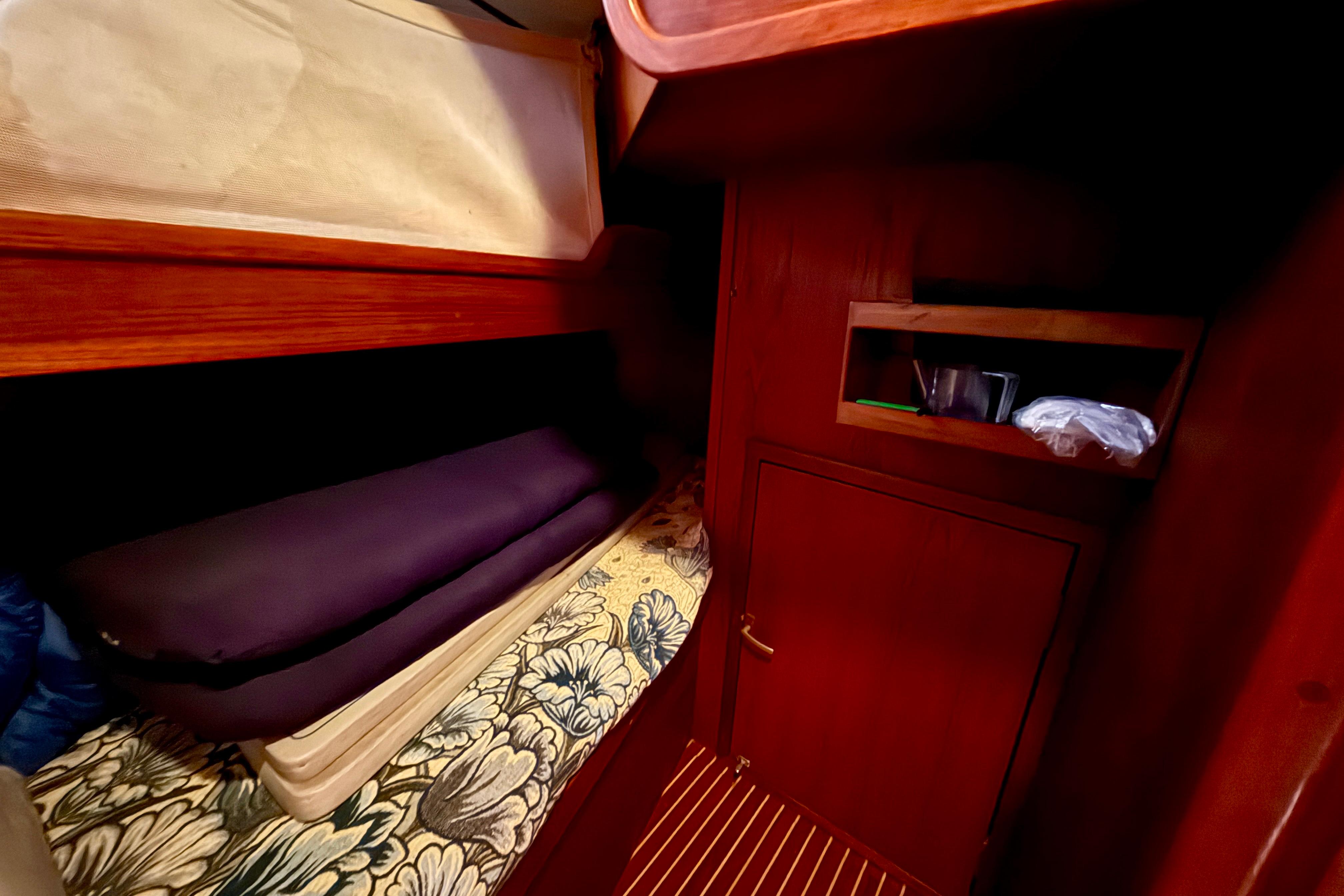 Cozy cabin interior of 1986 Nauticat 43 sailboat with wooden furnishings and floral bedding.