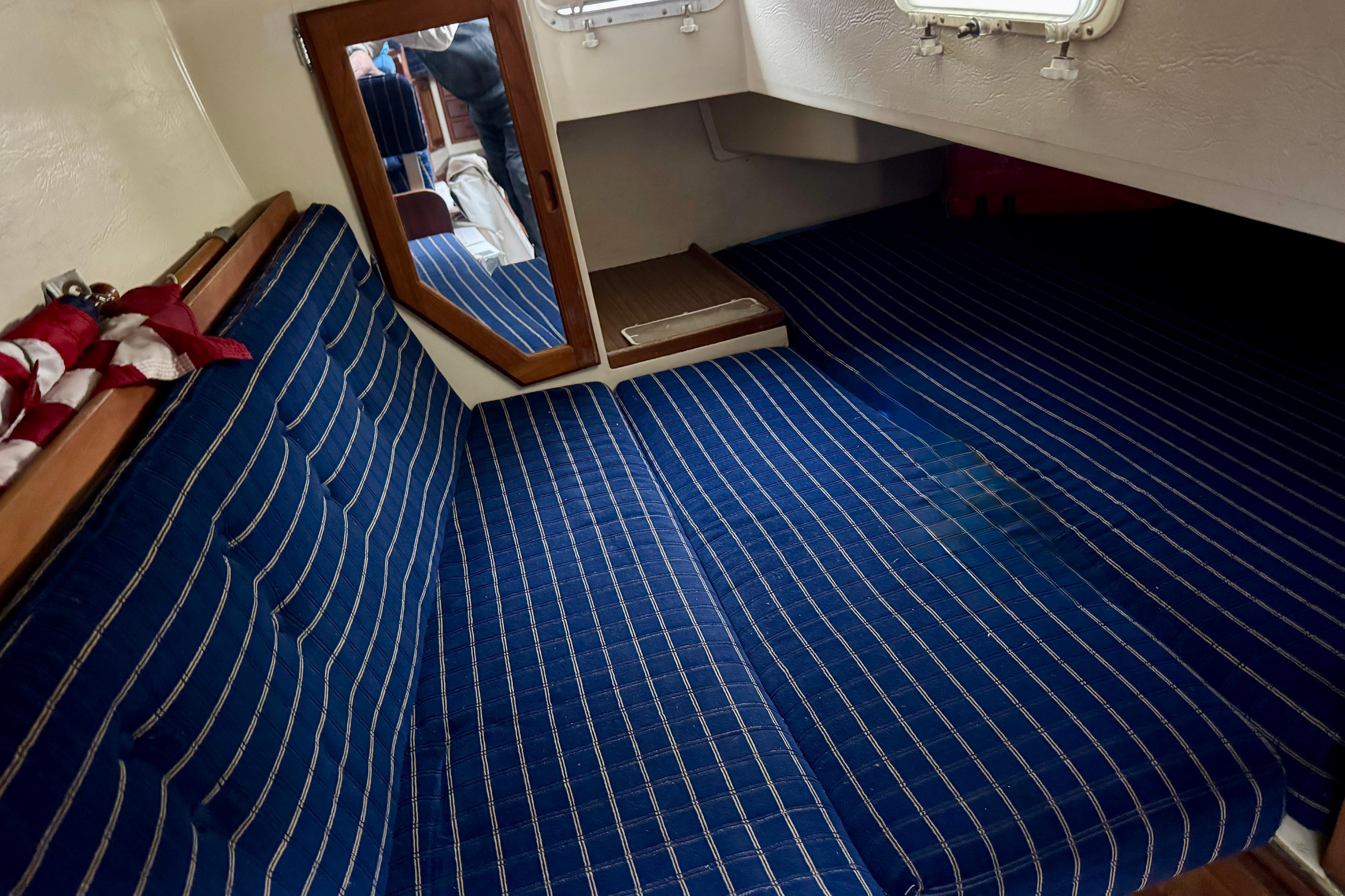Interior cabin of 1986 Catalina 36 sailboat with blue striped cushions and a mirror.